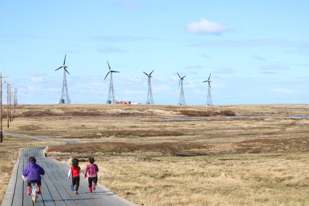 Second place: photo of two children running and one child biking on a boardwalk facing away from the camera. Tundra and five windmills in the background.
