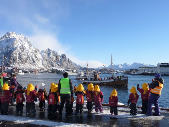 Third place: photo of adults and small children on shore, facing away toward a harbor with boats and snowcapped mountains in the background.